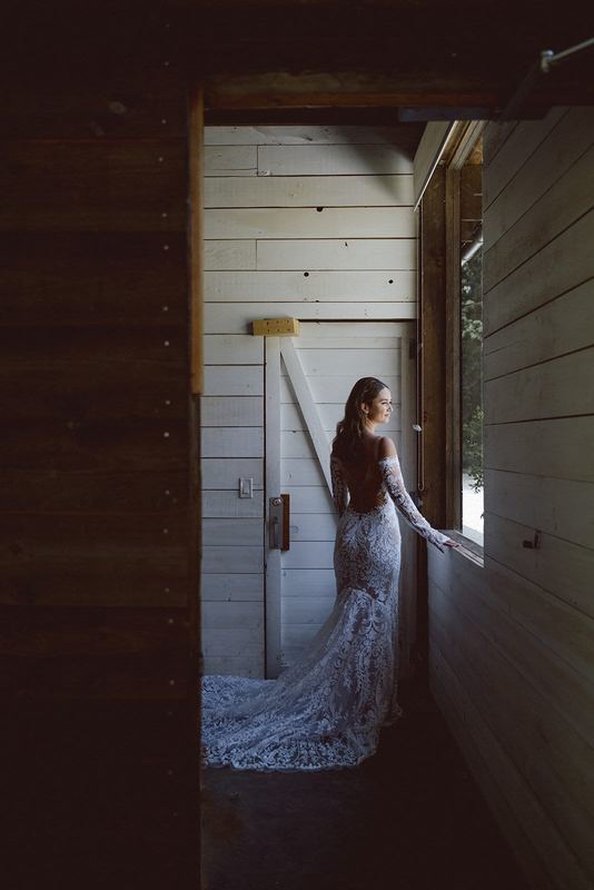 Bride with a long lace train looking out a cabin window