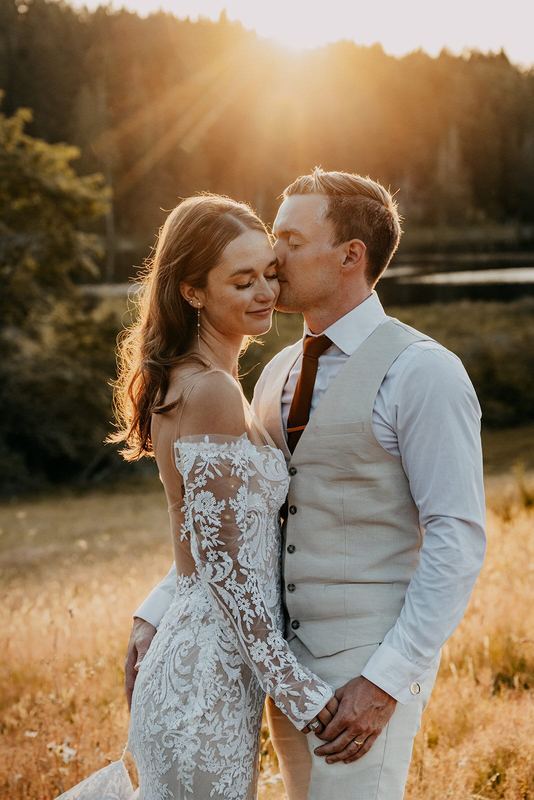 Golden-hour kiss on the bride's temple in a sunlit field