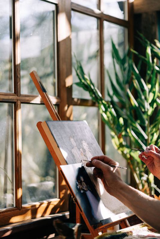 Hand painting a small canvas beside a sunlit studio window
