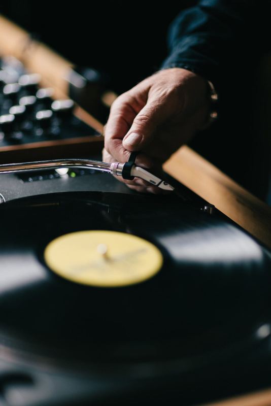Fingers on the tonearm above a yellow-label vinyl