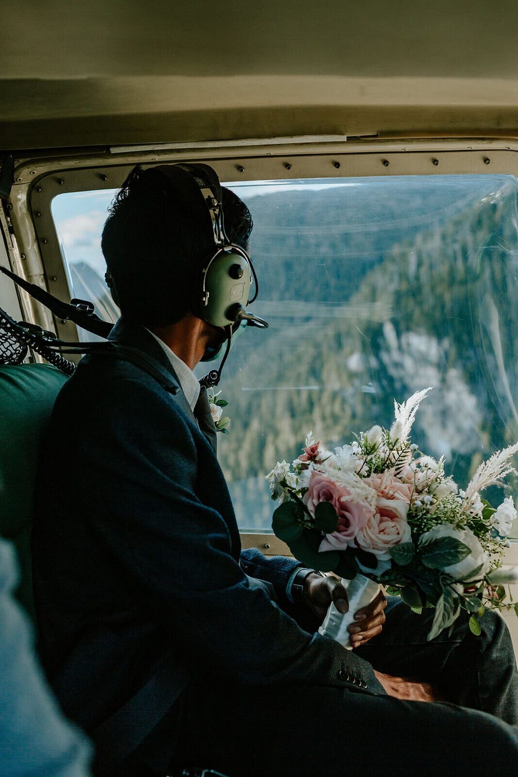 Groom in a helicopter headset carrying the bouquet over mountain cliffs