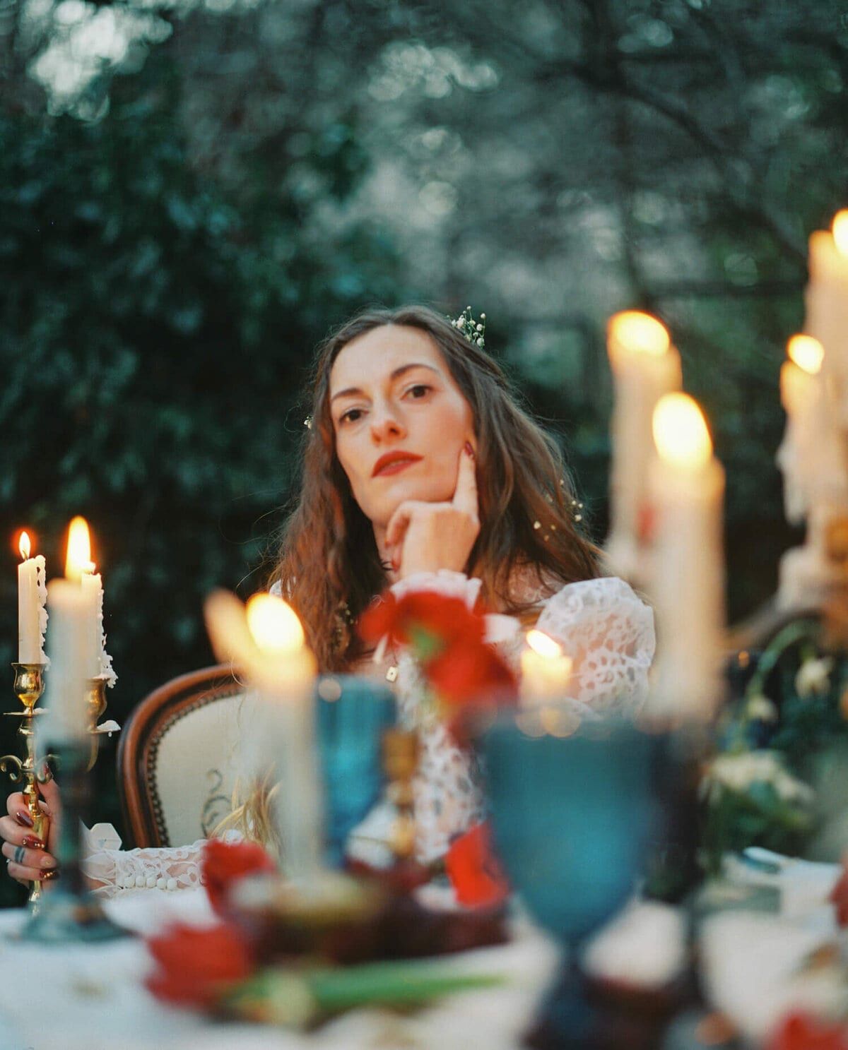 Pensive bride behind glowing taper candles and blue glass goblets
