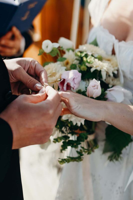Groom sliding a ring onto the bride's finger over a pastel bouquet