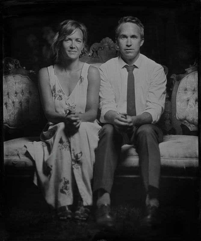 Couple in summer attire seated on a Victorian sofa, tintype